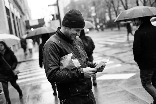 A man grinning at a note on a rainy street corner