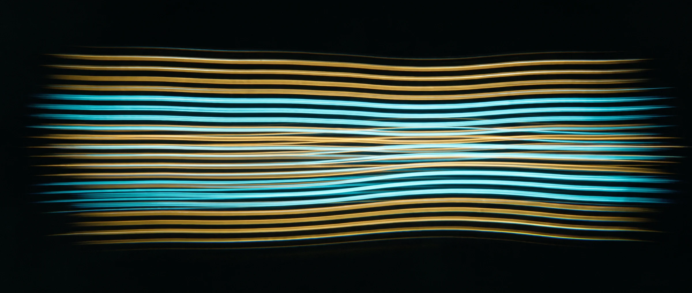 Parallel gold and cyan light trails stretched across a black frame
