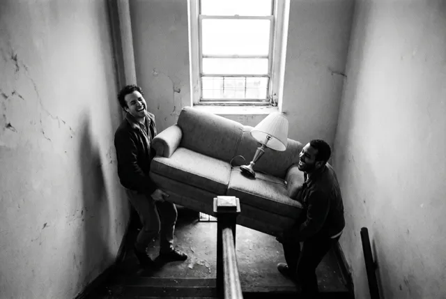 Two friends laughing as they carry a sofa up a stairwell