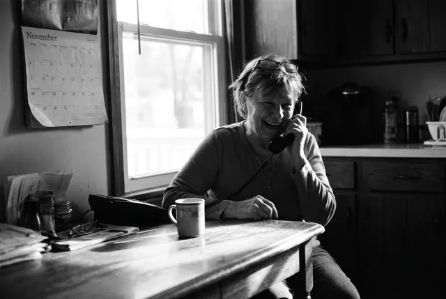 An older woman laughing on the phone at her kitchen table